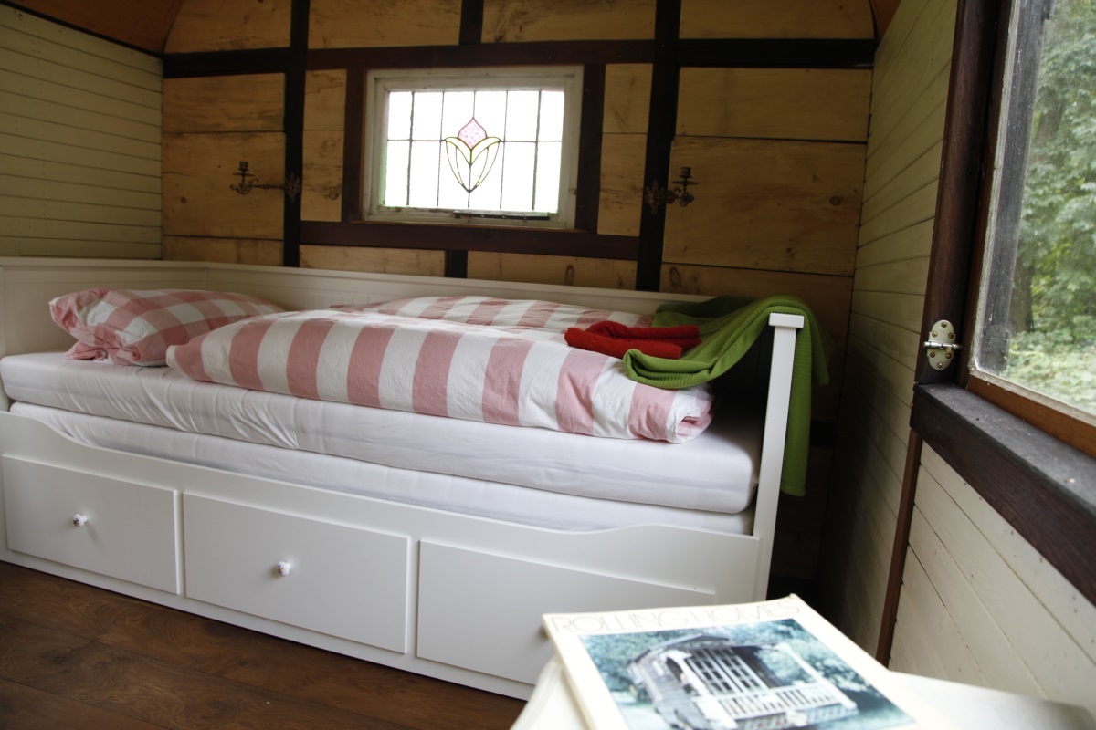 Helles Bett mit rosa-weißem Karostoff im Inneren des Zirkuswagens, Buntglasfenster